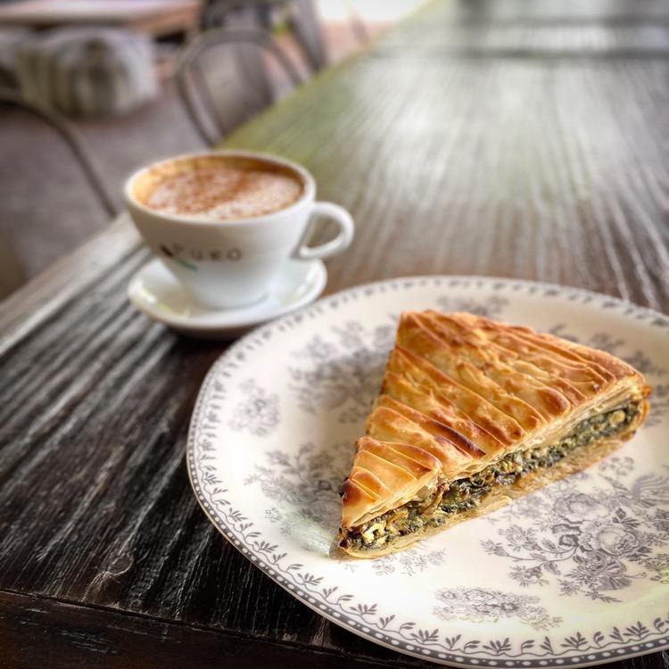 Espresso and a slice of spanakopita on a floral plate at Living Green Cafe